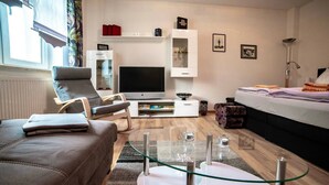A modern living room with a sofa, TV, glass coffee table, and a bed. - Apartment 'Moderne Ferienwohnung In Der Stadt' with Balcony and Wi-Fi (Forst/Lausitz)