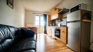 A compact living space with a sofa, kitchenette, and a view through a glass door. - Apartment 'Moderne Ferienwohnung In Der Stadt' with Balcony and Wi-Fi (Forst/Lausitz)