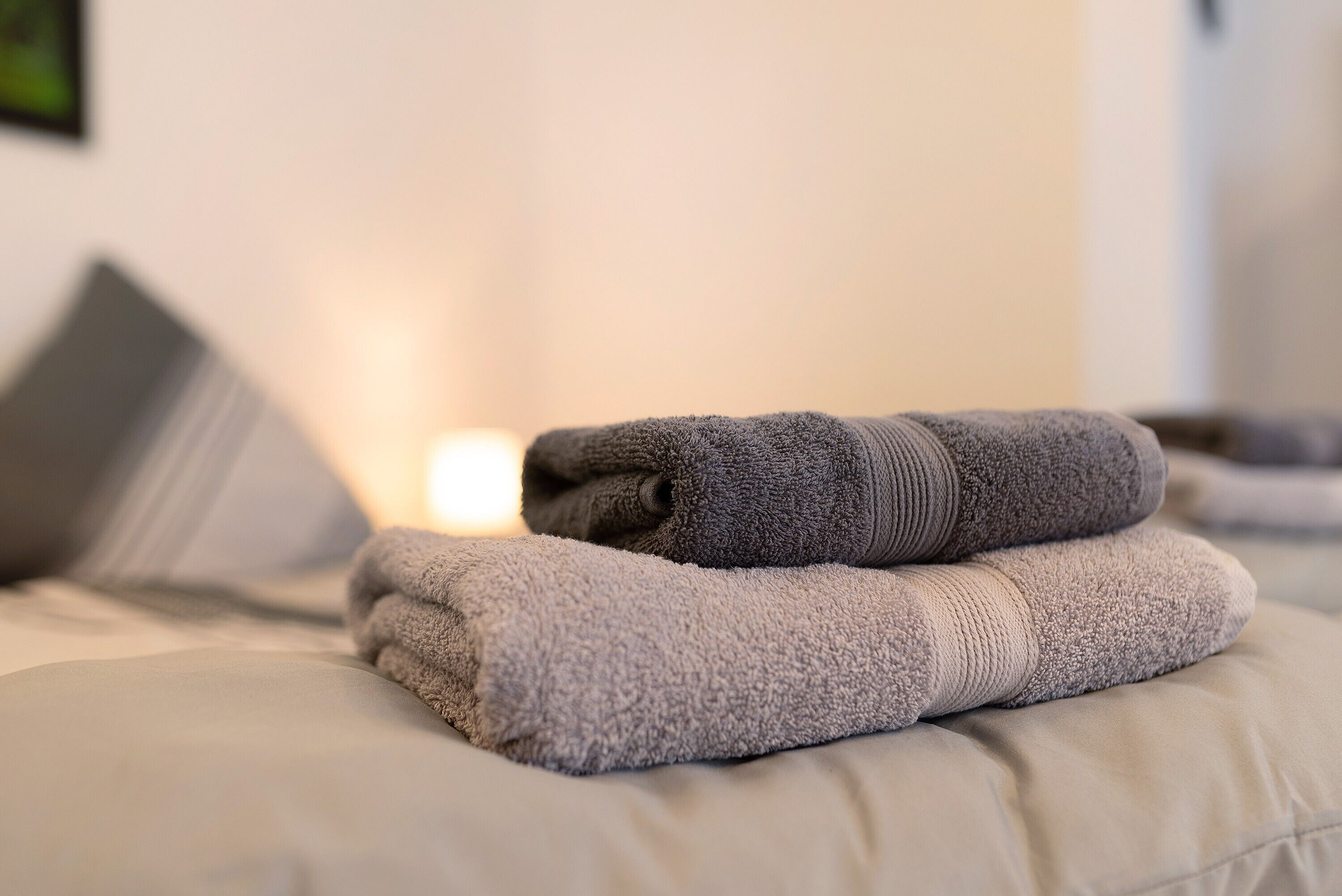 A neatly folded gray towel on a bed with a pillow.