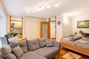 A modern living room with a sofa, a dining table with chairs, a kitchen area, and a bed with pillows. - Studio Apartment 'Schwarzwaldnestle' with Mountain View, Wi-Fi and Air Conditioning (Bad Wildbad)