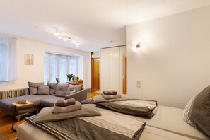 A modern room with a sofa, two beds, a radiator, and a wooden door. - Studio Apartment 'Schwarzwaldnestle' with Mountain View, Wi-Fi and Air Conditioning (Bad Wildbad)