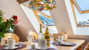Ein Esstisch gedeckt mit weißen Tassen, Untertassen und Tellern, einer Orangensaftflasche und einer Champagnerflasche.