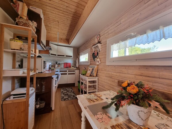Une cuisine chaleureuse aux murs en bois, une fenêtre ornée de rideaux en dentelle et une table agrémentée d’un centre de table floral.