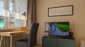 Una sala de estar con televisor, escritorio, silla, radiador y un cuadro enmarcado en la pared.