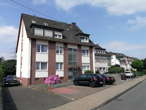 A multi-story residential building with a red and white facade, a front entrance, and a driveway with parked cars.