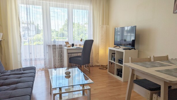 A living room with a sofa, a glass coffee table, a TV on a stand, a desk with a chair, and a bookshelf. - Holiday Apartment 'Haus Abendsonne Upper Floor Small' with Shared Terrace, Balcony and Wi-Fi (Koblenz)