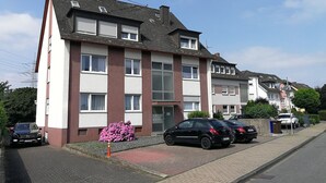 A multi-story residential building with a red and white facade, a gated entrance, and parked cars along the street. - Holiday Apartment 'Haus Abendsonne Upper Floor Small' with Shared Terrace, Balcony and Wi-Fi (Koblenz)