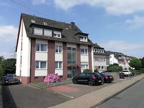 Un immeuble résidentiel à plusieurs étages, doté d’une façade rouge et blanche, d’une entrée sécurisée et de voitures garées le long de la rue.