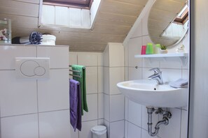 Une salle de bain avec un lavabo blanc, un miroir, un porte-serviettes avec des serviettes vertes et violettes, et une petite étagère contenant des articles de toilette.
