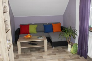 Un salon comprenant un canapé, une table basse, une plante en pot et une petite table sur laquelle se trouve un panier de fruits.
