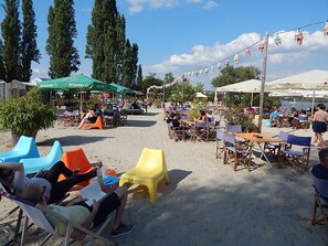 Espace extérieur aménagé avec des tables et des chaises, un auvent vert et un sol sablonneux.