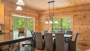 Interior de una cabaña de madera con comedor, encimera de piedra y ventanas amplias.