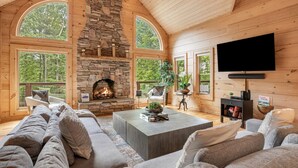 Una sala de estar acogedora con chimenea de piedra, ventanas amplias y un televisor de pantalla plana.