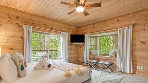Un dormitorio de cabaña de madera con una cama, un ventilador de techo y un televisor.