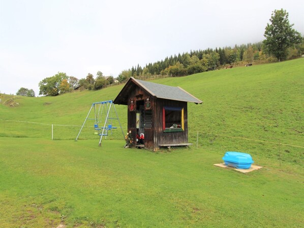 Uma pequena cabana de madeira com um balanço em um campo gramado.