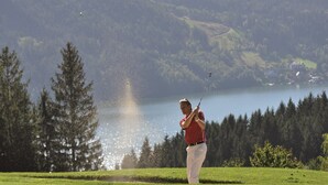 Un golfeur sur un terrain de golf, avec un lac et une forêt en arrière-plan.