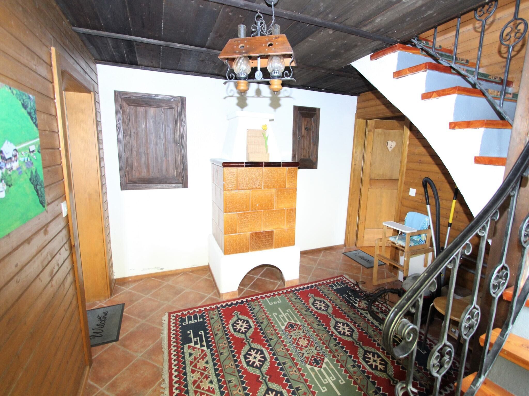 Interior de madera con suelo de baldosas, chimenea, escalera y lámpara colgante.