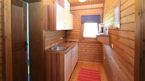 Une petite cabane en bois comprenant un coin cuisine, une petite fenêtre avec vue et un tapis rouge sur le sol.
