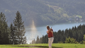 Un golfeur sur un terrain de golf, avec un lac et une forêt en arrière-plan.