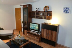 A modern living room with a flat-screen TV, wooden shelving, a sofa, and a coffee table.