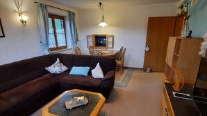 Een woonkamer met een bank, een salontafel, een eettafel met stoelen en een kast.
