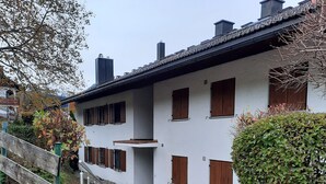 Een gebouw met een stenen trap die leidt naar een houten deur, omringd door groen en een heldere lucht.