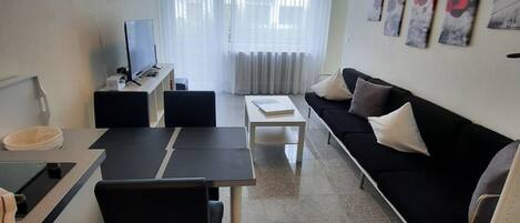 A modern living room with a dining area, a sofa, a TV, and artwork on the wall.