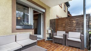 Un patio al aire libre con mobiliario de mimbre, una puerta corrediza de vidrio y una cerca de madera.