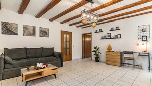 Una sala de estar con sofá, mesa de centro, escritorio de madera y techo con vigas a la vista.