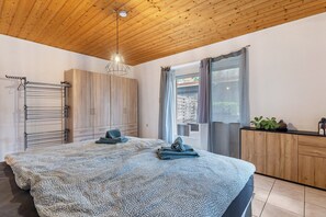 Une chambre avec un plafond en bois, un lit recouvert d’une couvre-lit à motifs, un étendoir et une armoire en bois.
