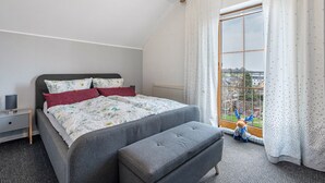 A bedroom with a bed, a bedside table, a window with curtains, and a view of the outside. - Holiday Apartment 'Omatina' with Balcony and Wi-Fi (Bannewitz)