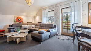 A modern living room with a sectional sofa, a coffee table, and a dining area with a table and chairs. - Holiday Apartment 'Omatina' with Balcony and Wi-Fi (Bannewitz)