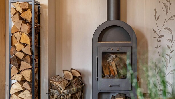A wood-burning stove, a stack of firewood, and a basket of logs. - Holiday Apartment 'Omatina' with Balcony and Wi-Fi (Bannewitz)