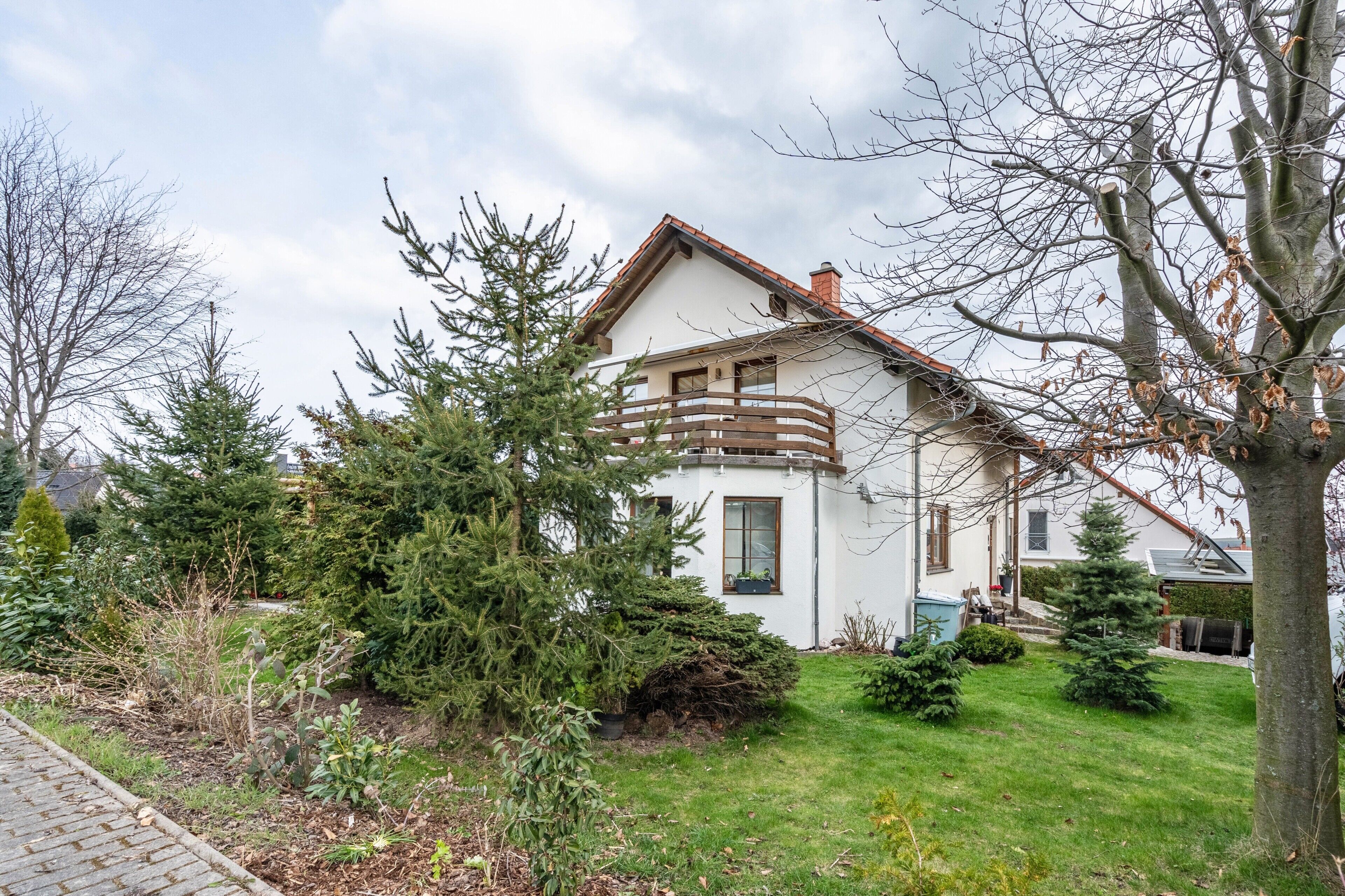Ein zweigeschossiges Haus mit Balkon, umgeben von einem gepflegten Garten und Bäumen.