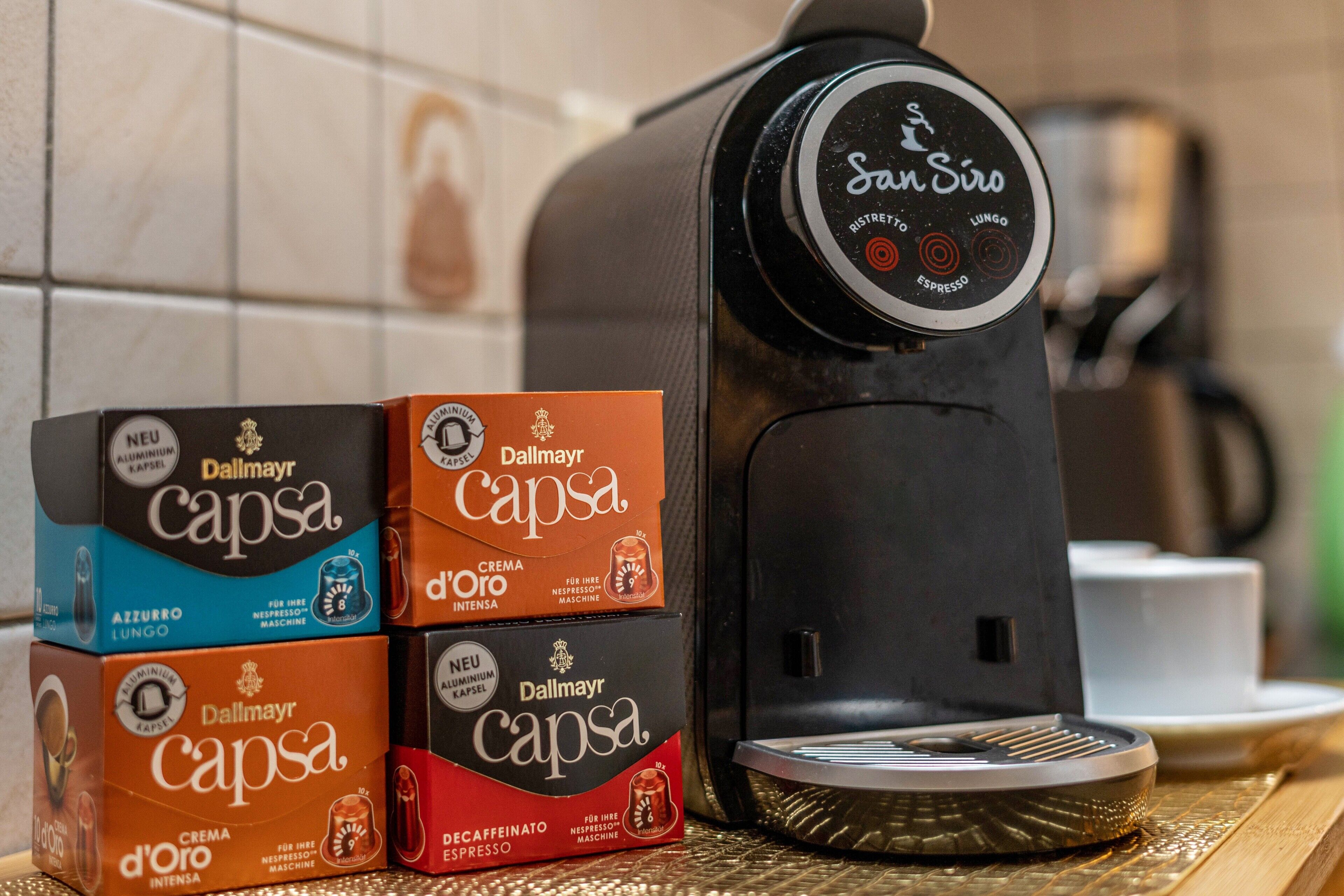 En kaffemaskine med digitalt display, ved siden af kasser med Dalmary Capsa kaffekapsler.