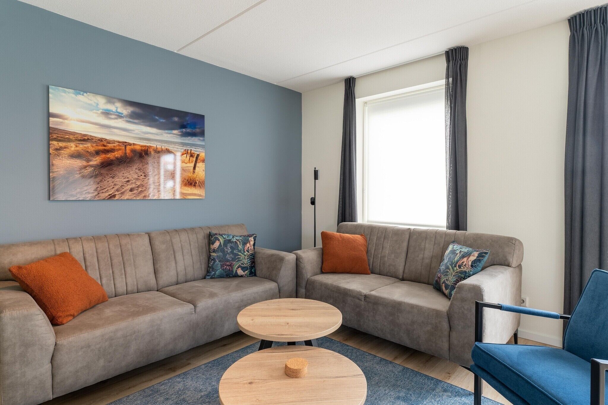 A modern living room with a beige sectional sofa, a blue armchair, and a round wooden coffee table.