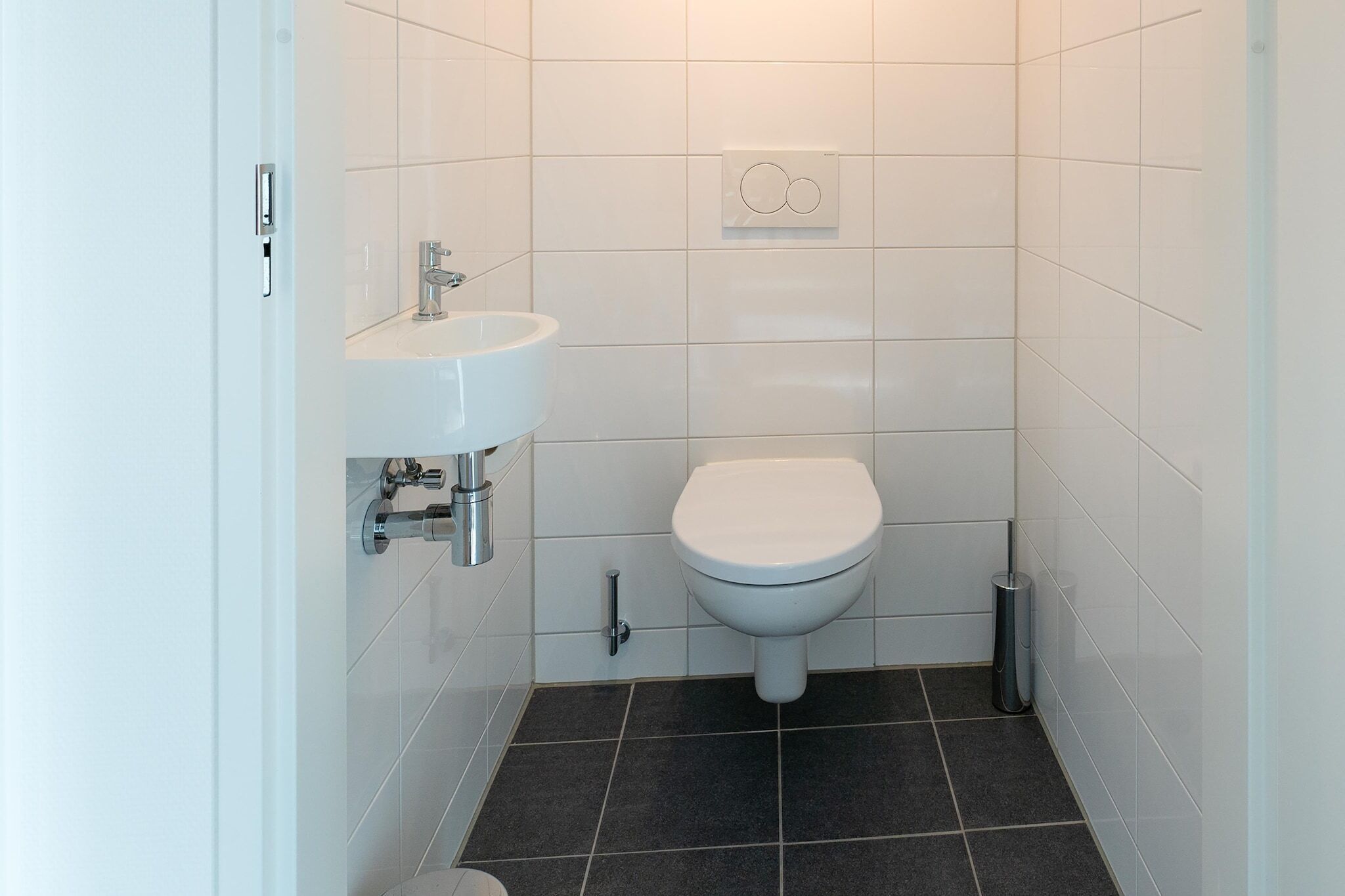 A small, modern bathroom with white tiles, a white sink, and a toilet.