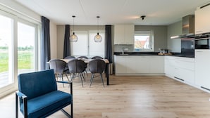 Een moderne keuken met witte kasten, een zwart aanrechtblad en een inbouwoven. Er is een zithoek met een tafel en stoelen, en een blauwe bank op de voorgrond.