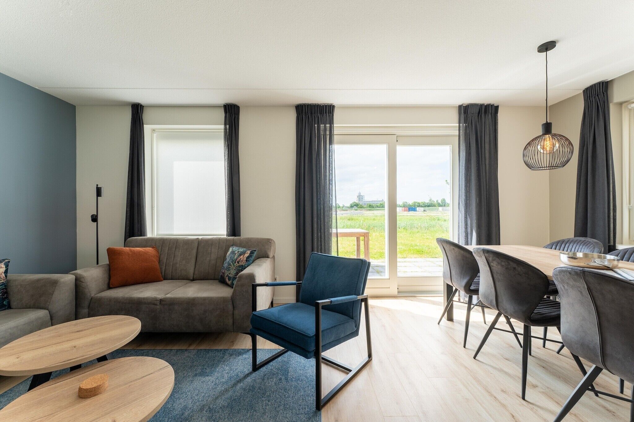 Una sala de estar moderna con un sofá, una silla azul, una mesa de comedor con sillas y vistas al exterior.