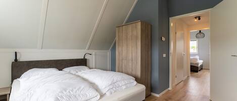 Un dormitorio con cama, armario de madera y un pasillo que conduce a otra habitación.