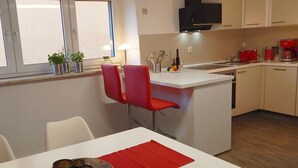 Een kleine keuken met een eethoek, een raam met zonwering en een rode stoel.