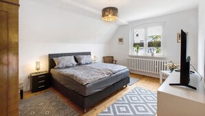 Quarto com cama, mesas de cabeceira, escrivaninha e janela.