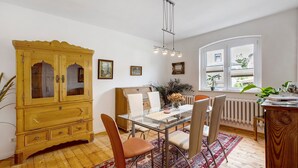 Uma sala de jantar com mesa de vidro, cadeiras, um armário de madeira e janela com vista.