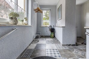 Ein Badezimmer mit Fliesenboden, einem Fenster mit Spitzenvorhängen, einem Hängeständer und einer Vase mit Blumen.