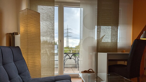 Una sala de estar moderna con un sofá, una mesa de centro de vidrio y vista al exterior a través de un ventanal corredero.