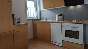 Una cocina moderna con armarios de madera, lavavajillas integrado, estufa y ventana con cortinas.
