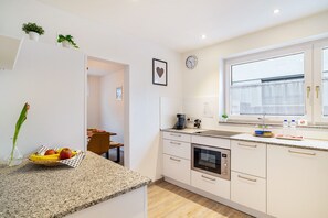 Une cuisine moderne avec des meubles blancs, un plan de travail en granit, une horloge et une fenêtre avec des rideaux.