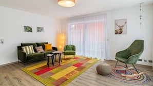 Un salon moderne avec un canapé, un fauteuil, une petite table et un tapis coloré.