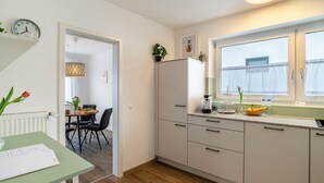 Une cuisine moderne avec des meubles blancs, un réfrigérateur, un coin repas avec une table et des chaises, et une horloge au mur.