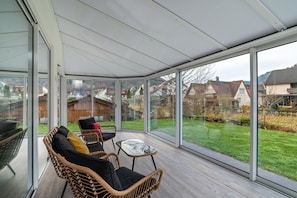 A conservatory with wicker furniture, large glass doors, and a view of a residential area.